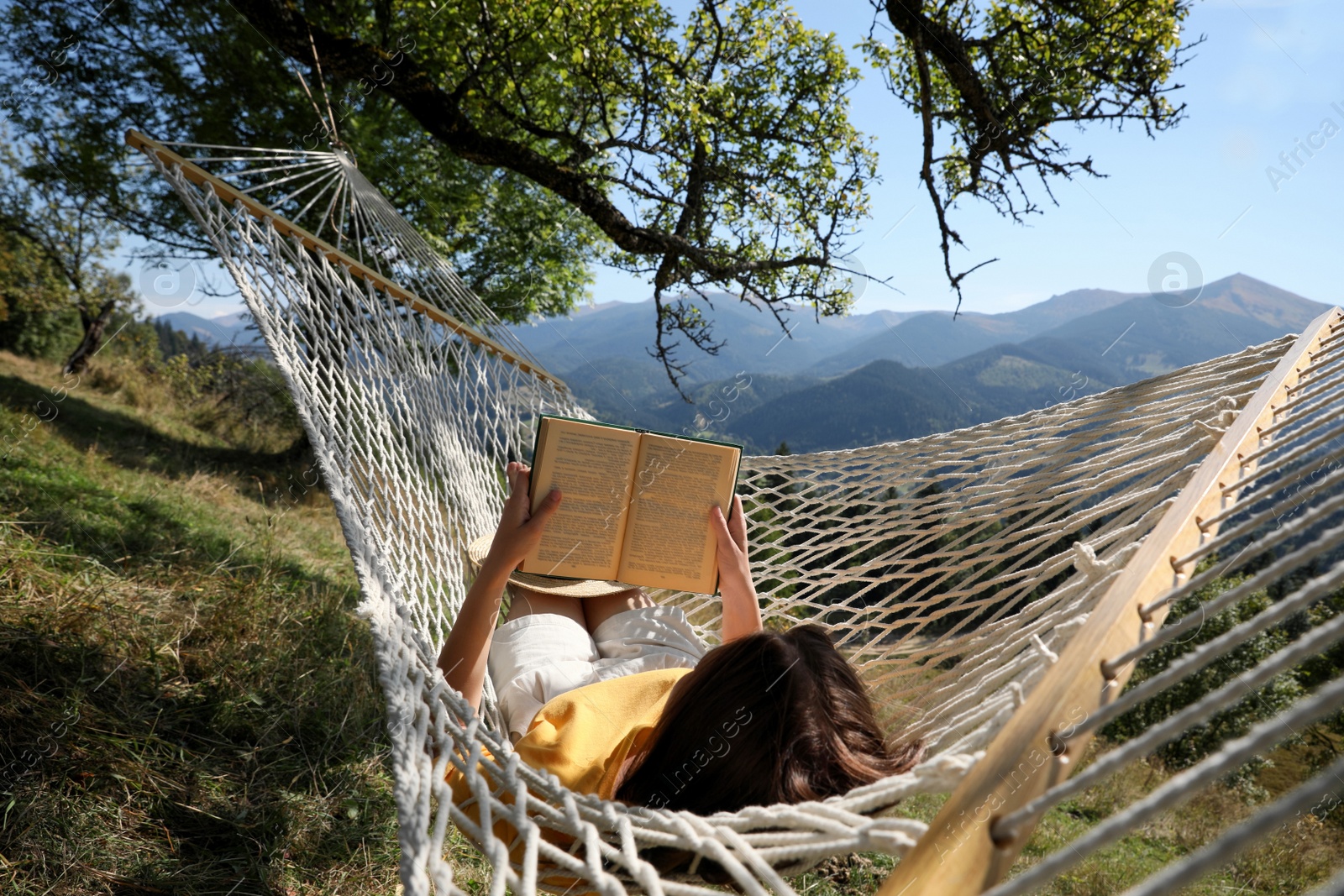 Photo of Young woman reading book in hammock outdoors on sunny day