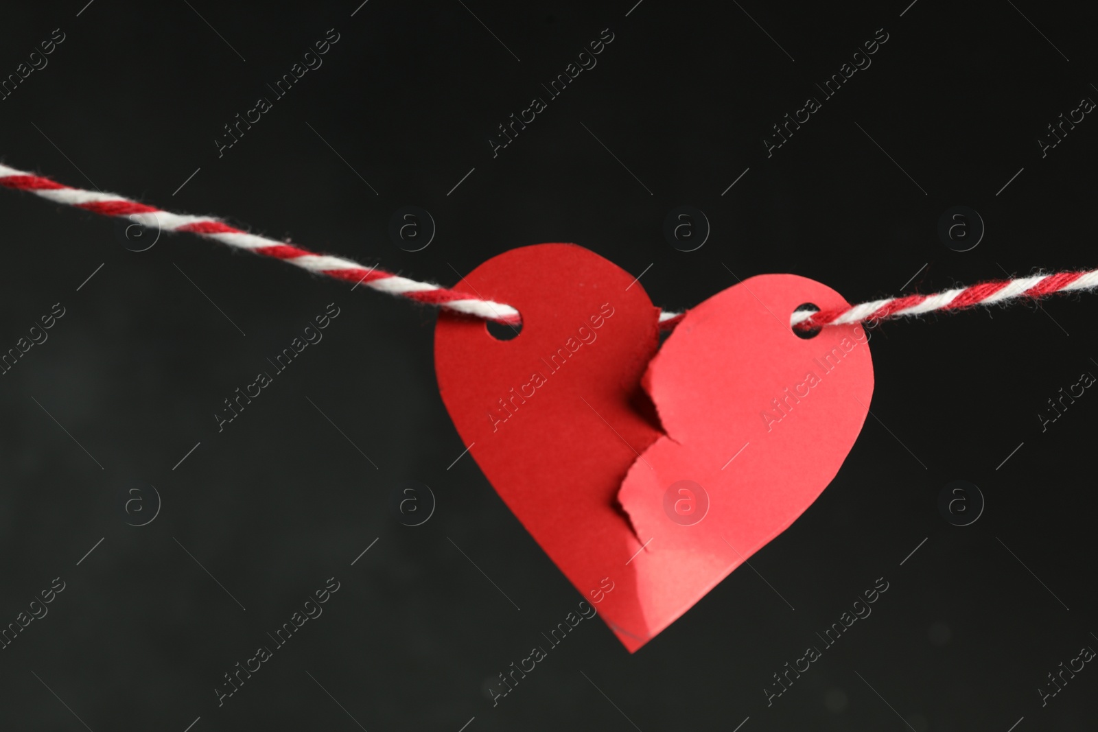 Photo of Broken red paper heart on rope against black background. Relationship problems concept