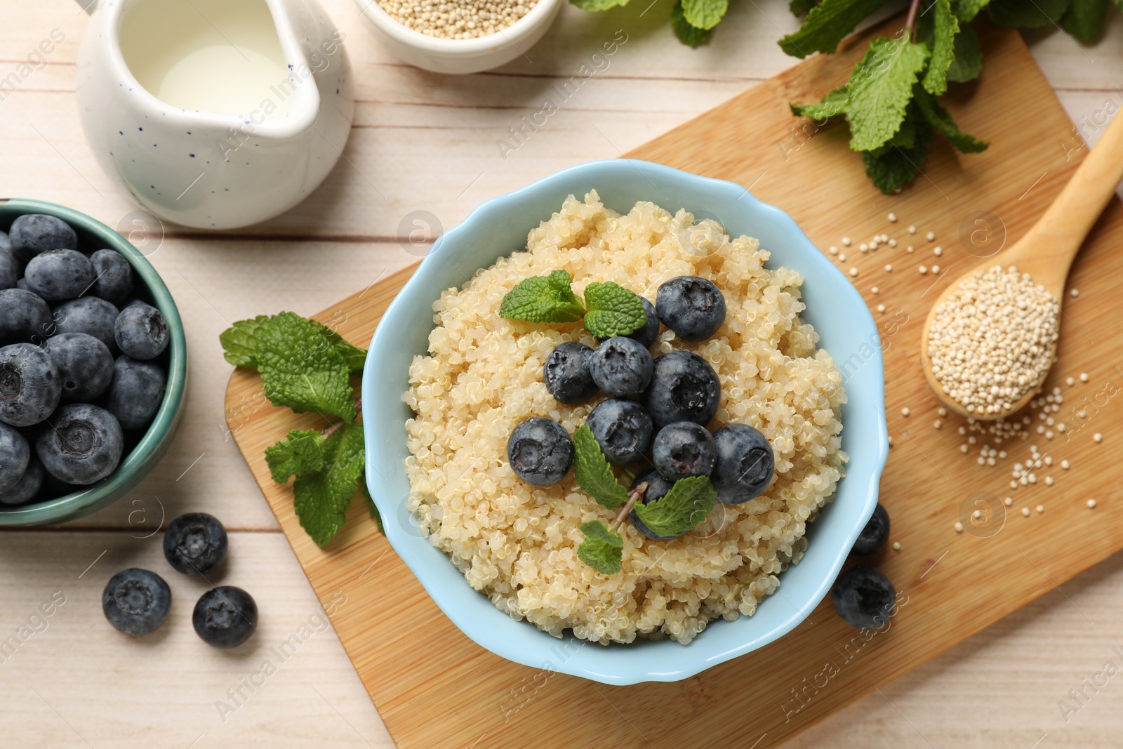 Photo of Tasty quinoa porridge with blueberries and mint in bowl on light wooden table, flat lay