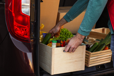 Photo of Courier taking crate with products from car, closeup. Food delivery service