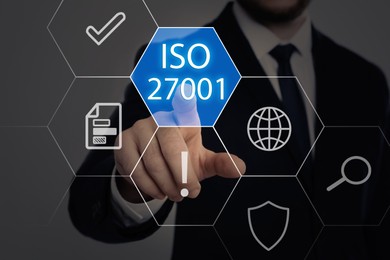 Image of Businessman pointing at virtual icon with text ISO 27001 on dark background, closeup. Quality management system  