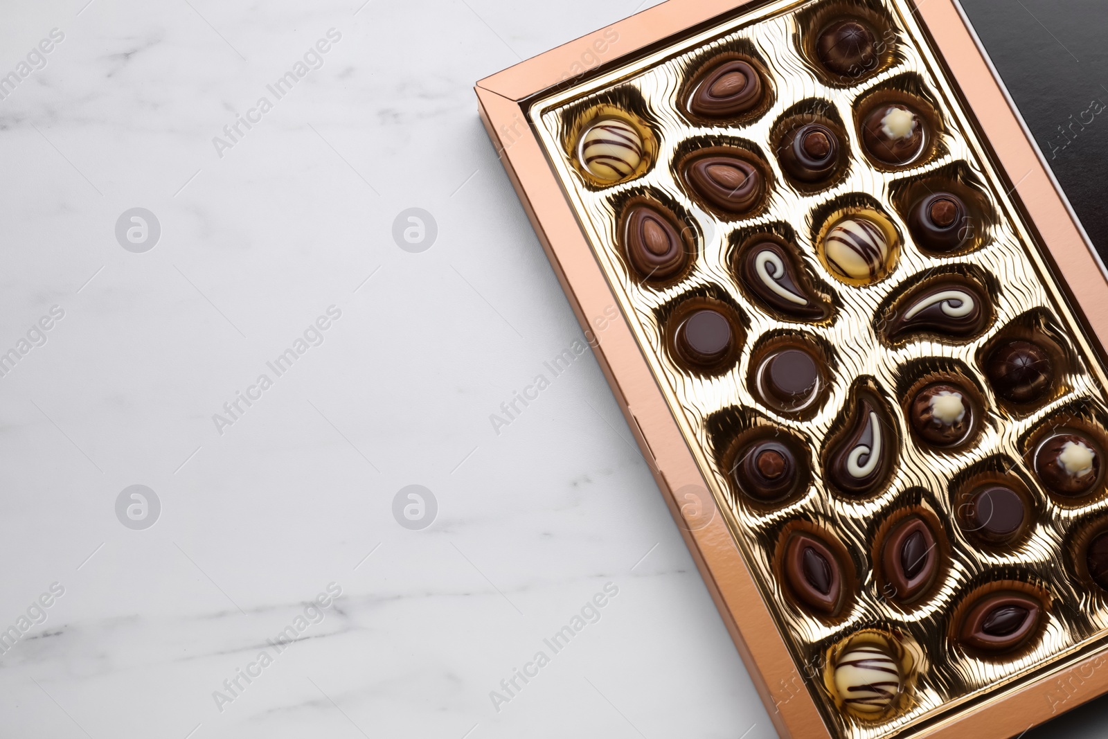 Photo of Box of delicious chocolate candies on white marble table, top view. Space for text