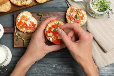 Photo of Woman preparing bruschetta with salmon at dark grey wooden table, top view