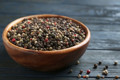 Mix of peppercorns in bowl on dark wooden table, closeup