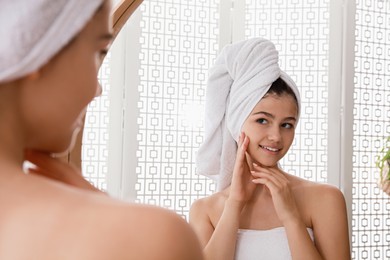 Beautiful teenage girl with towels near mirror in bathroom