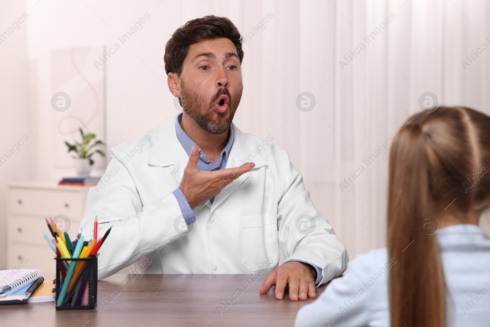 Photo of Dyslexia treatment. Speech therapist working with girl at table in room