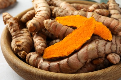 Bowl with whole and cut turmeric roots on table, closeup