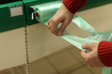 Photo of Man taking plastic bag from holder in supermarket, closeup