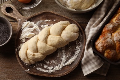 Photo of Raw braided bread and ingredients on wooden table, flat lay. Traditional Shabbat challah
