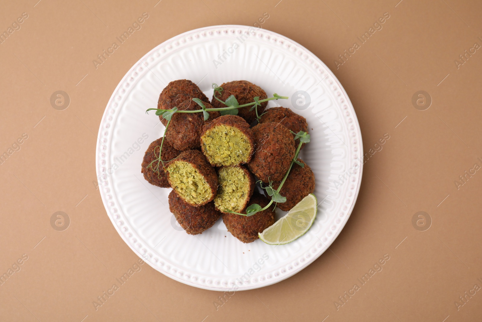 Photo of Delicious falafel balls, lime slice and microgreens on pale brown background, top view