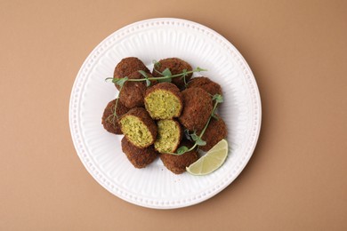 Delicious falafel balls, lime slice and microgreens on pale brown background, top view