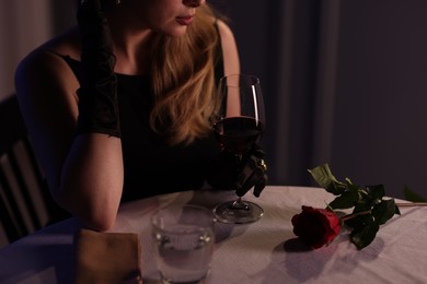 Photo of Elegant young woman with glass of wine at table indoors in evening, closeup