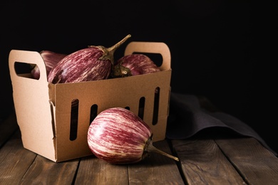 Photo of Ripe purple eggplants and cardboard box on wooden table. Space for text