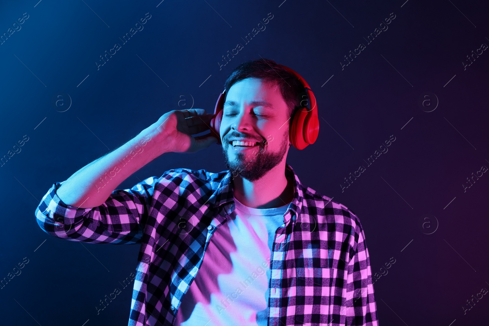 Photo of Happy man in headphones enjoying music in neon lights against dark blue background