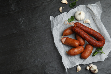 Delicious smoked sausages with garlic and parsley on black table, flat lay