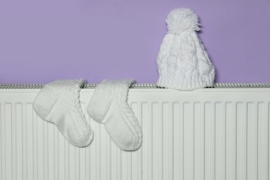 Photo of Knitted socks and hat on heating radiator near violet wall