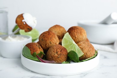 Photo of Delicious falafel balls with herbs and lime on white marble table