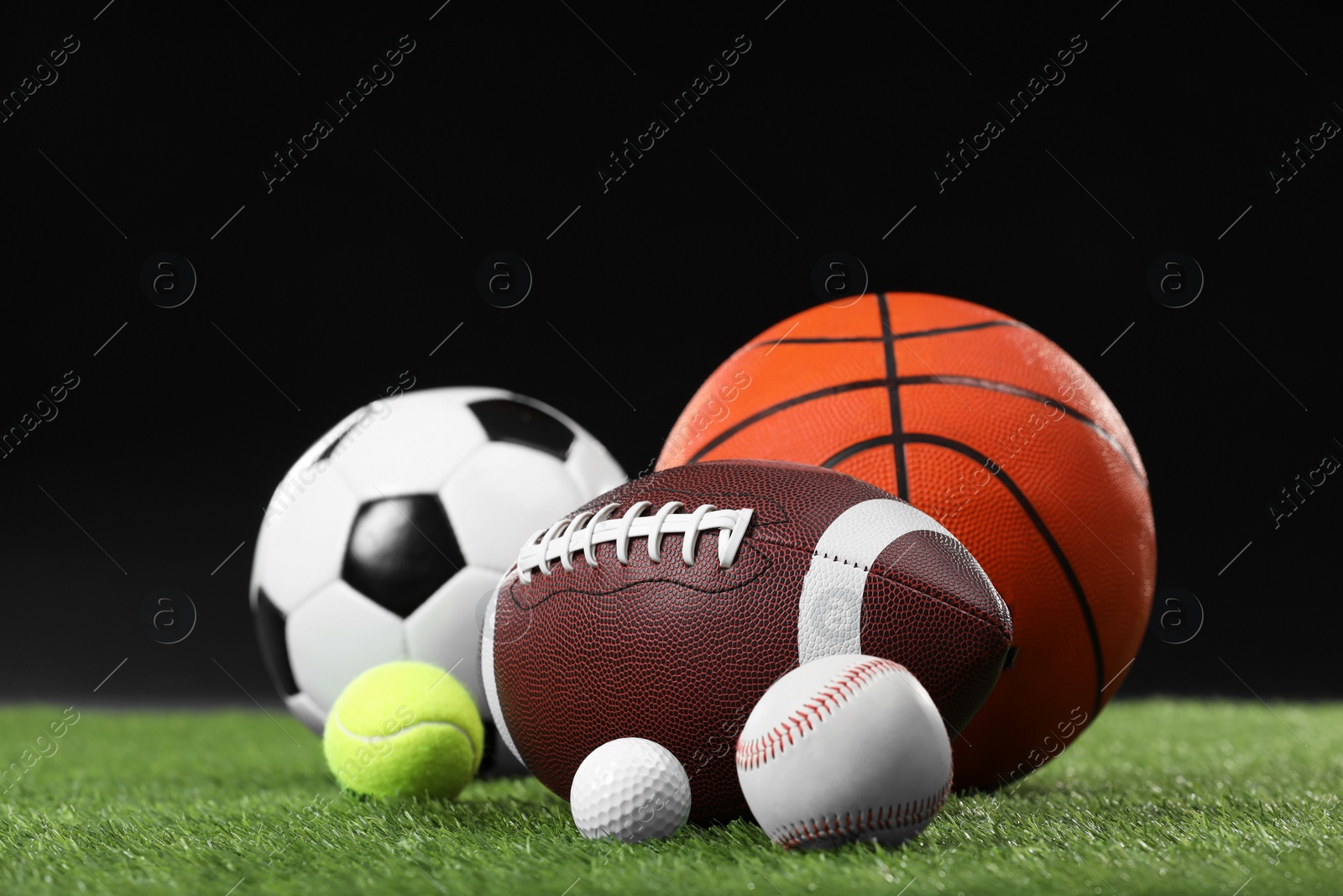 Photo of Many different sports balls on green grass against black background