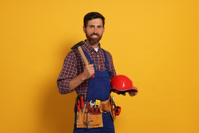 Professional builder in uniform with hammer and tool belt on yellow background