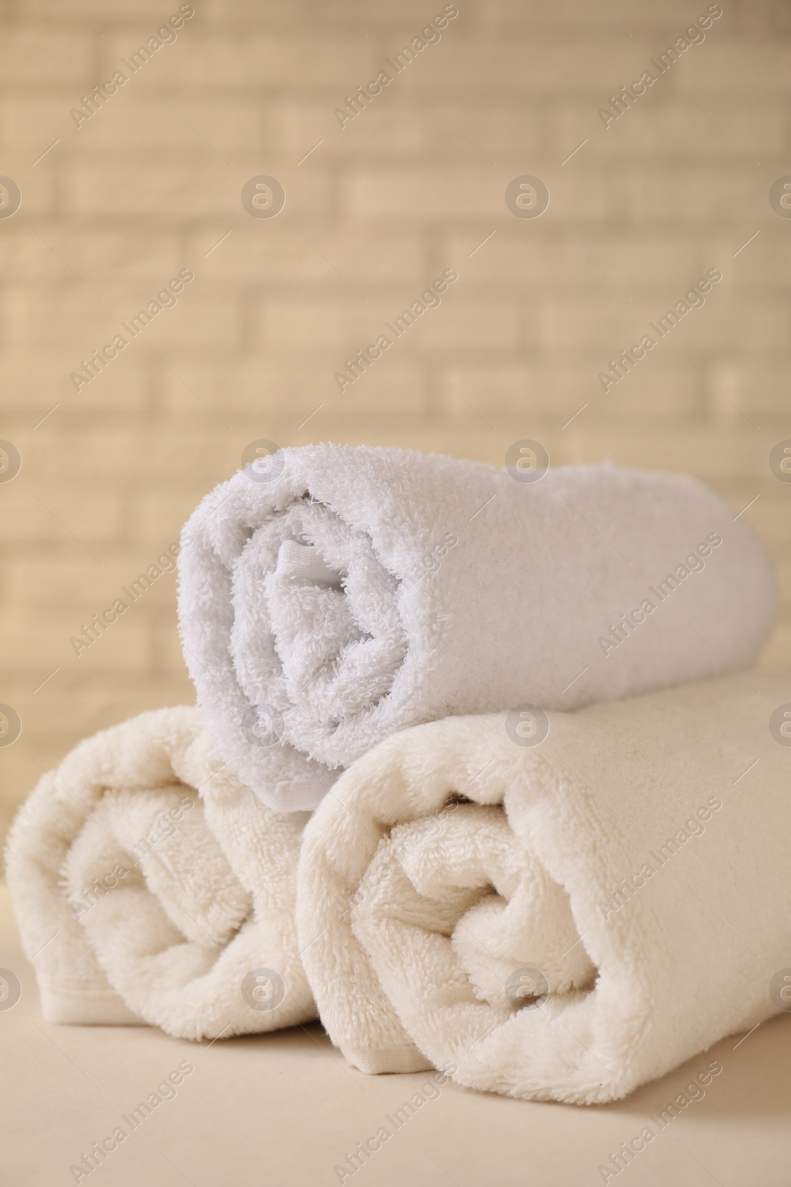 Photo of Rolled terry towels on white table near brick wall indoors, closeup. Space for text