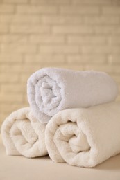 Rolled terry towels on white table near brick wall indoors, closeup. Space for text