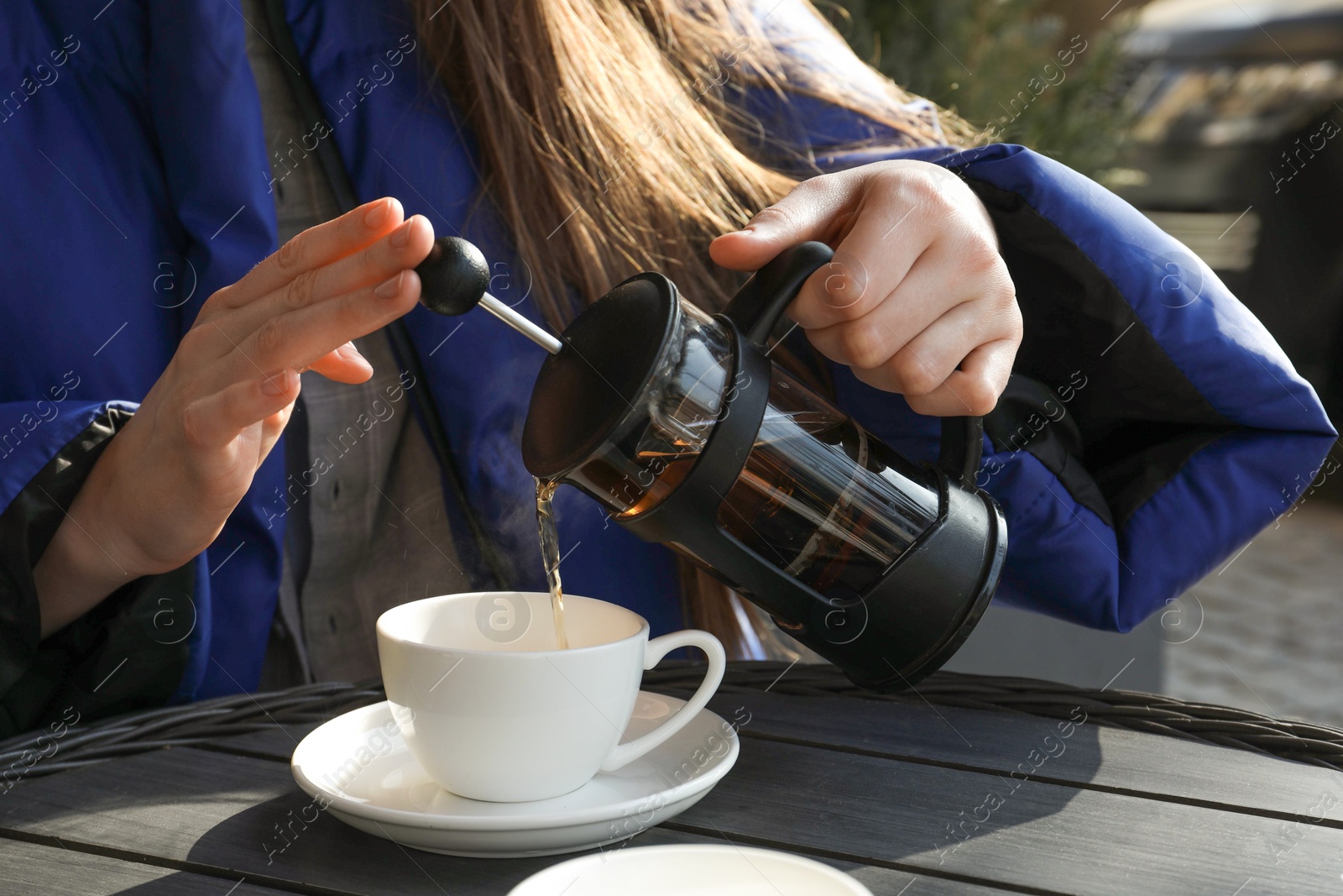 Photo of Woman pouring tea into cup at black wooden table in outdoor cafe, closeup