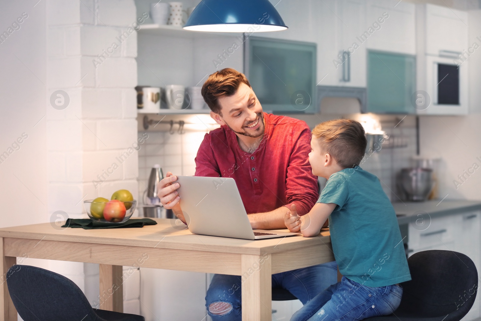 Photo of Little boy and his dad using laptop at home