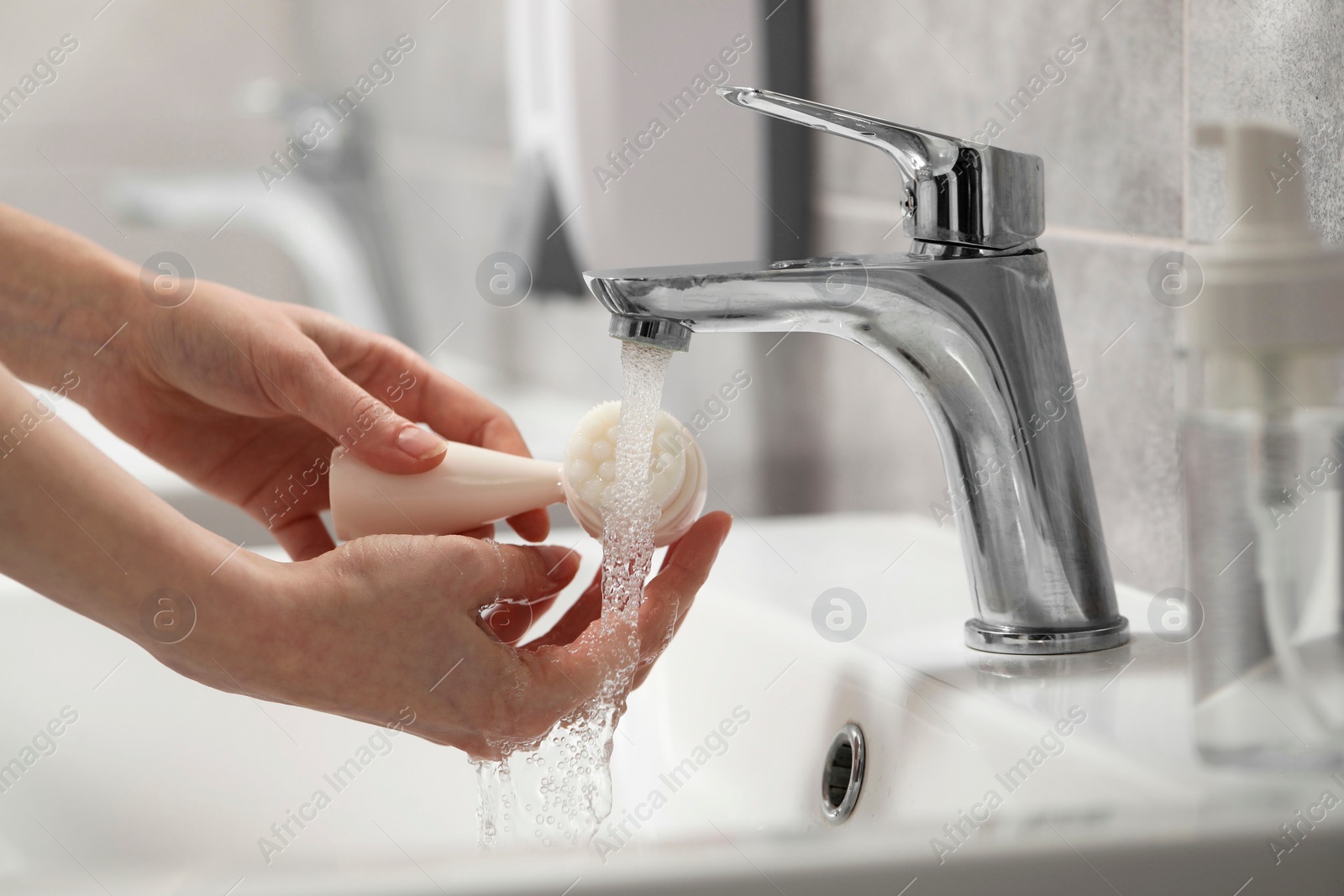 Photo of Young woman washing facial brush in bathroom, closeup