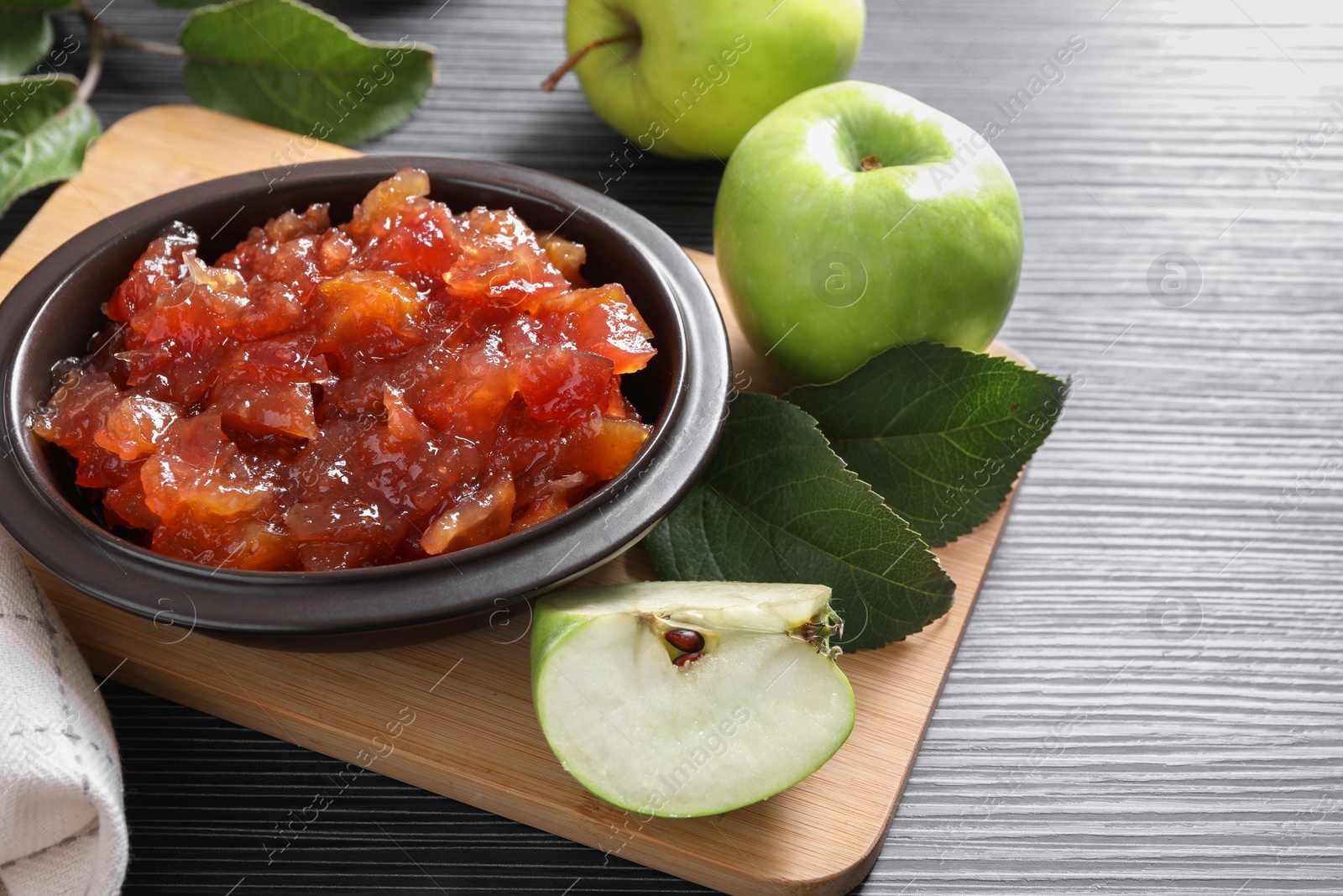 Photo of Bowl of delicious apple jam and fresh fruits on black wooden table