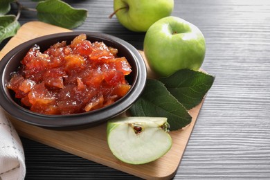 Photo of Bowl of delicious apple jam and fresh fruits on black wooden table