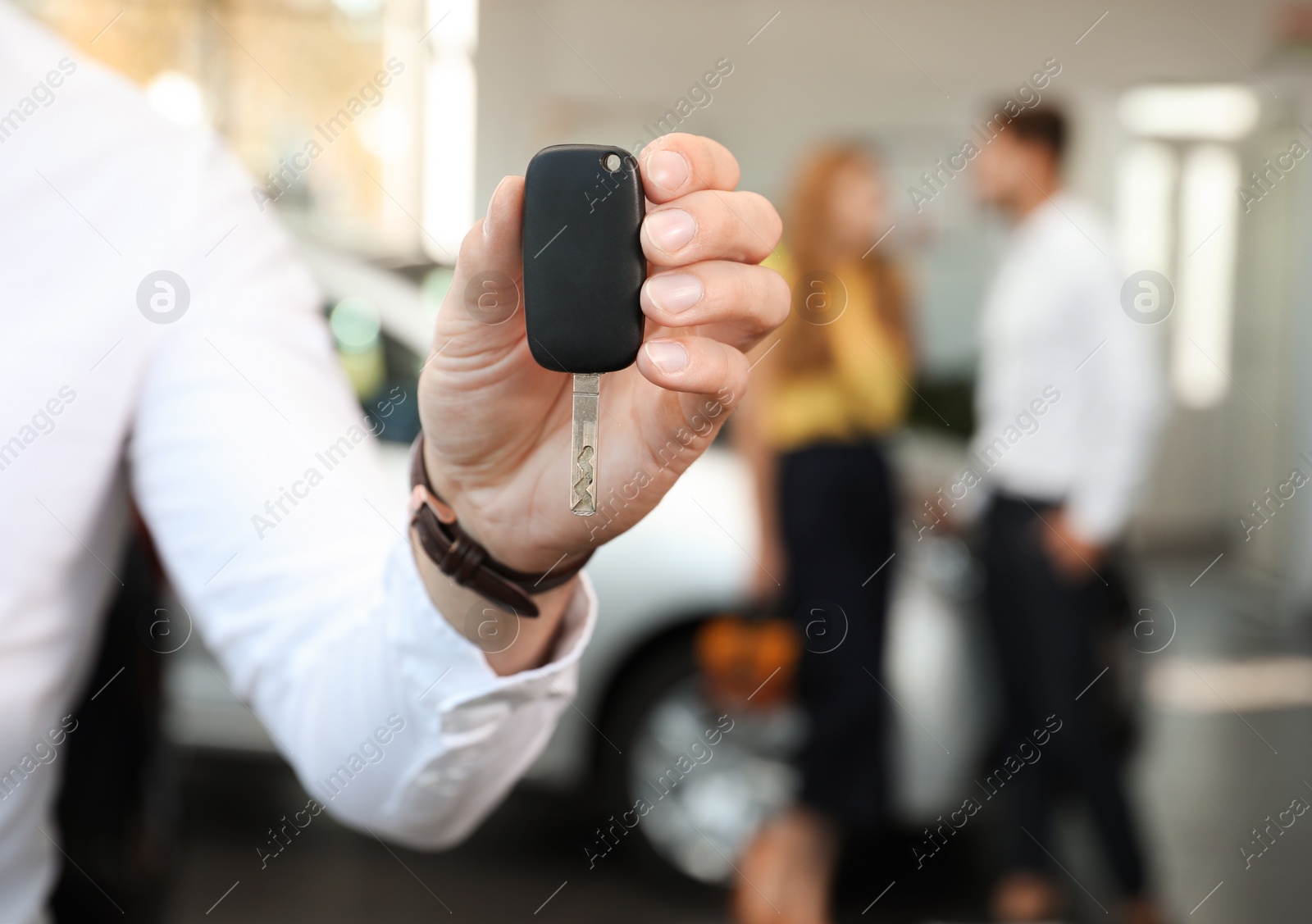 Photo of Young salesman with car key in dealership, closeup