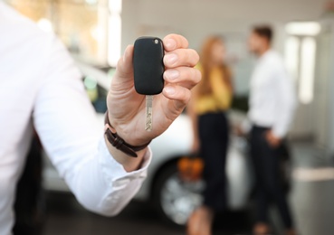 Photo of Young salesman with car key in dealership, closeup