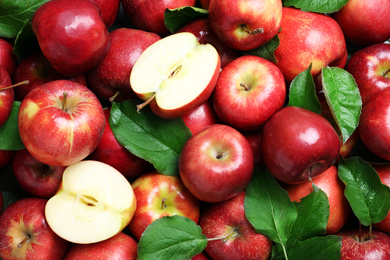 Photo of Pile of tasty red apples with leaves as background, top view