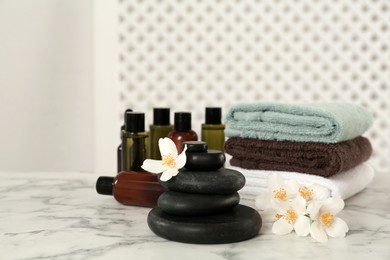 Photo of Black spa stones, beautiful jasmine flowers, towels and skin care products on white marble table