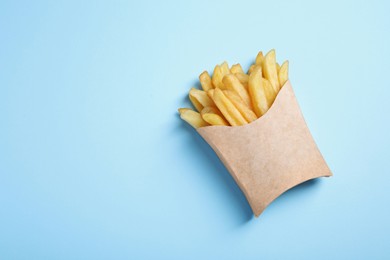 Photo of Paper cup with French fries on light blue table, top view. Space for text