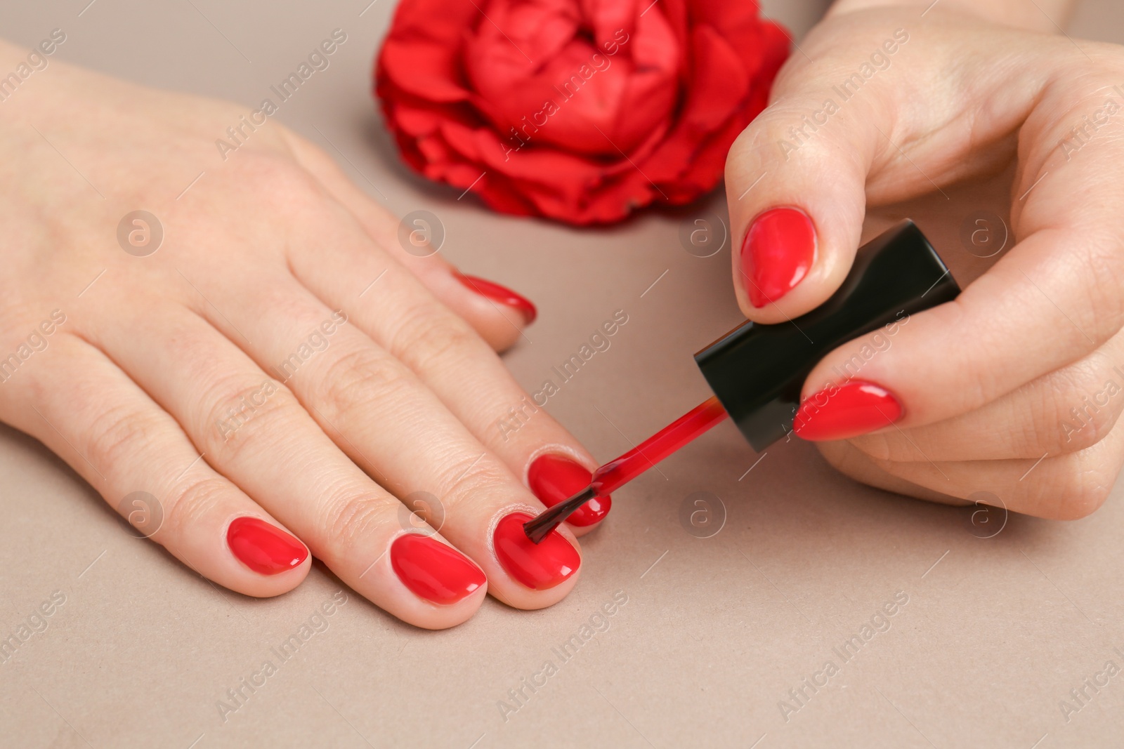 Photo of Woman painting nails with red polish on beige background, closeup