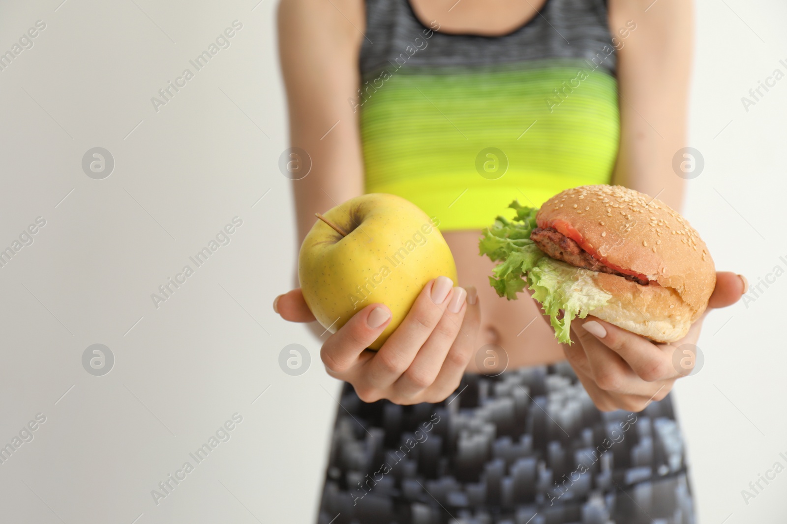 Photo of Woman holding tasty sandwich and fresh apple on light background. Choice between diet and unhealthy food