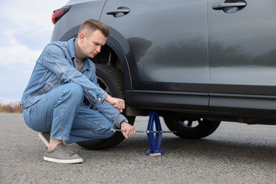 Young man changing tire of car on roadside