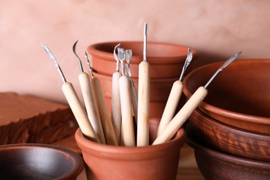 Photo of Set of different crafting tools and clay dishes on table in workshop, closeup