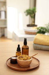 Photo of Dry flowers, bottles of essential oils and jar with cream on wooden table indoors, space for text. Spa time
