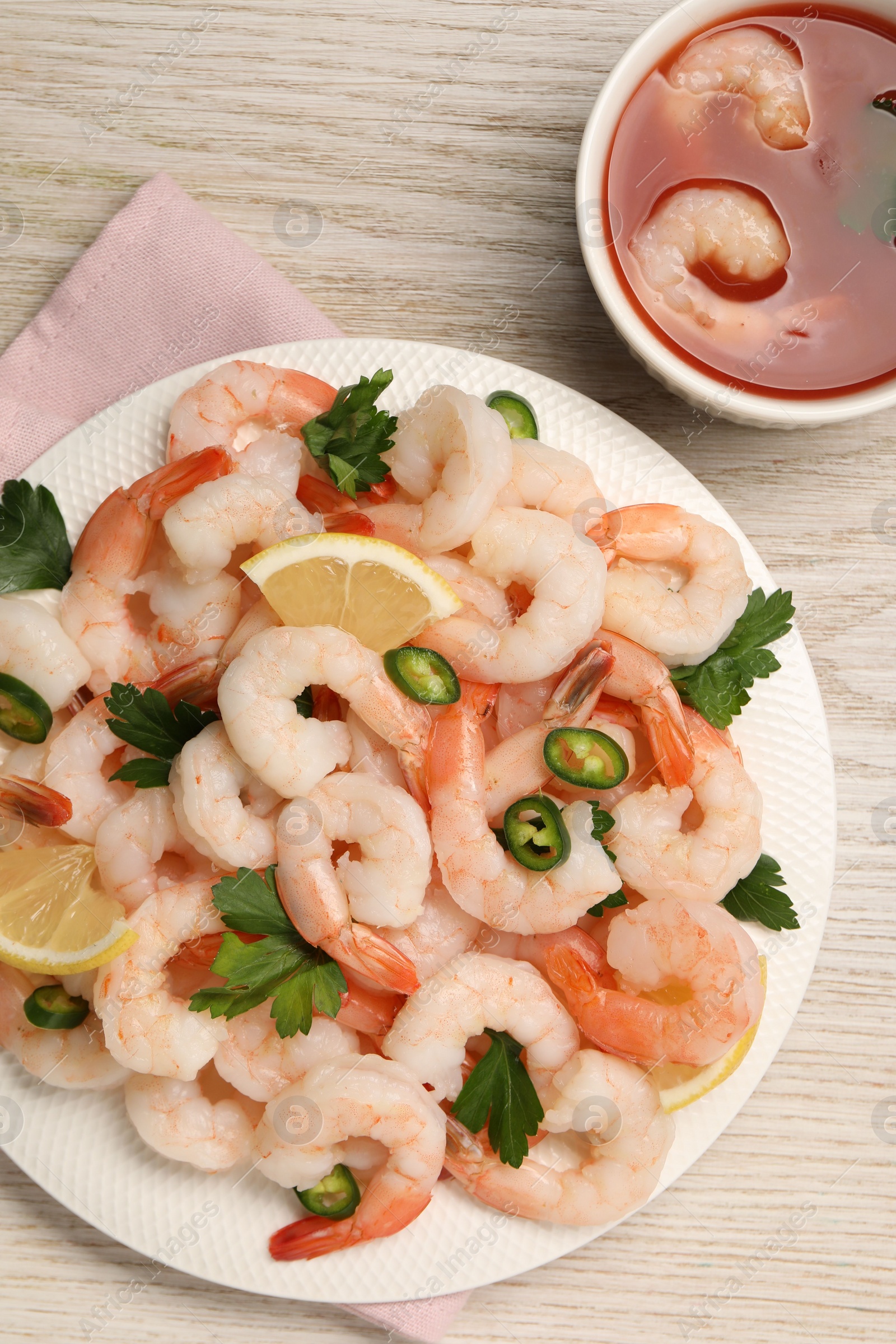 Photo of Tasty boiled shrimps with cocktail sauce, chili, parsley and lemon on light wooden table, flat lay