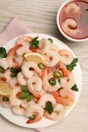 Tasty boiled shrimps with cocktail sauce, chili, parsley and lemon on light wooden table, flat lay