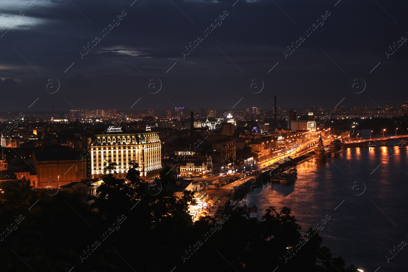 Photo of KYIV, UKRAINE - MAY 21, 2019: Beautiful view of night city with illuminated Fairmont Grand Hotel and other buildings near river