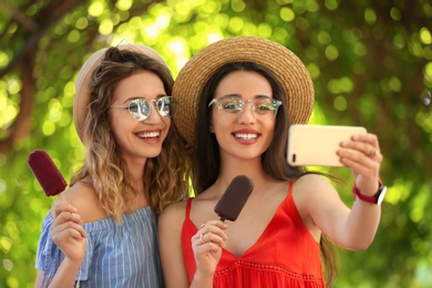 Photo of Happy young women with delicious ice creams taking selfie outdoors