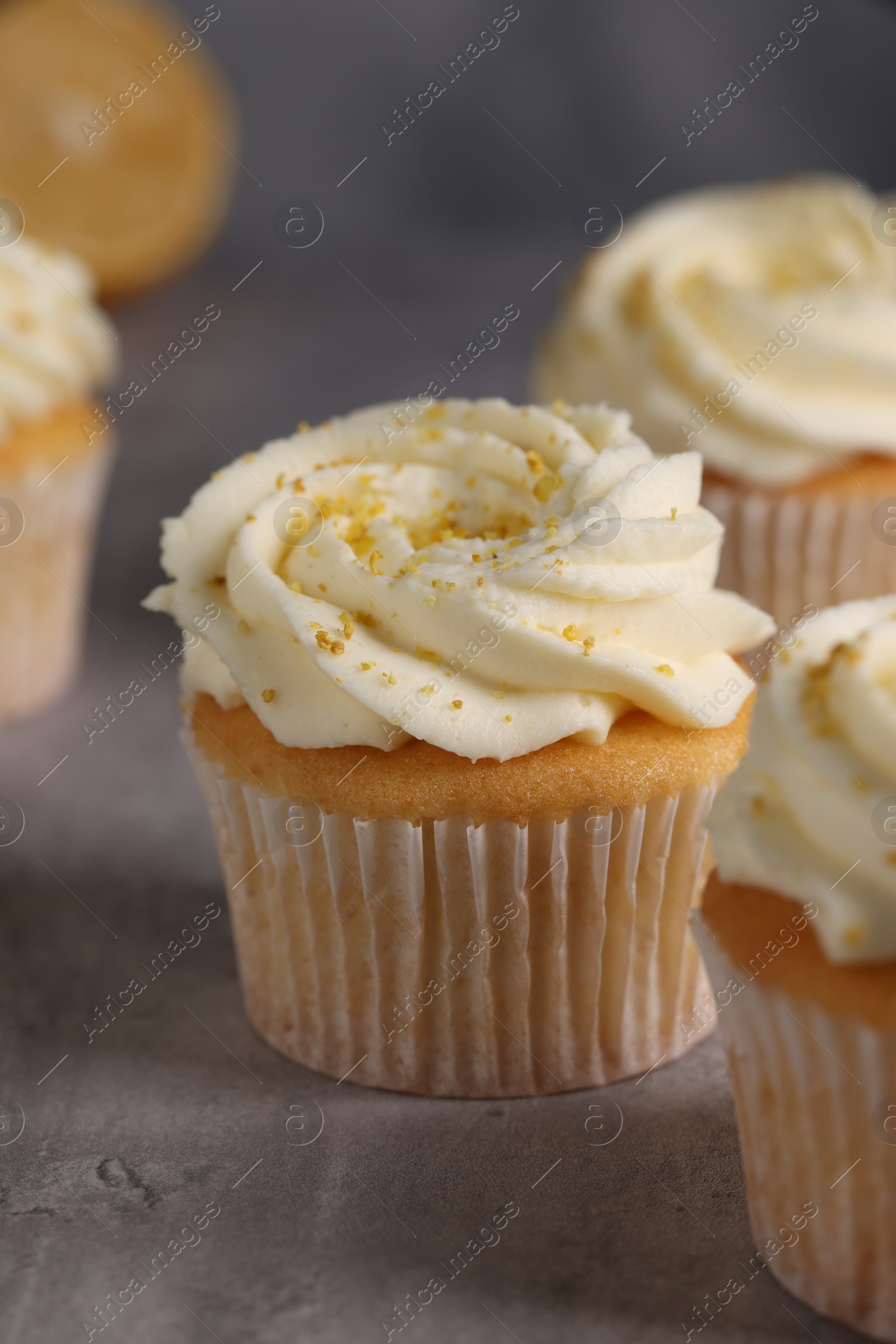 Photo of Delicious cupcakes with white cream and lemon zest on gray table, closeup