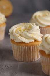 Delicious cupcakes with white cream and lemon zest on gray table, closeup