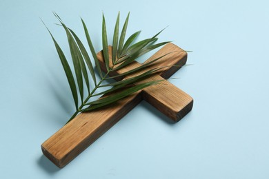 Photo of Wooden cross and palm leaf on light blue background. Easter attributes