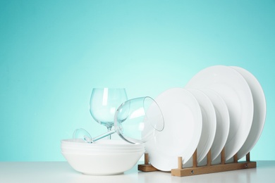 Photo of Set of clean dishes and glasses on table against color background