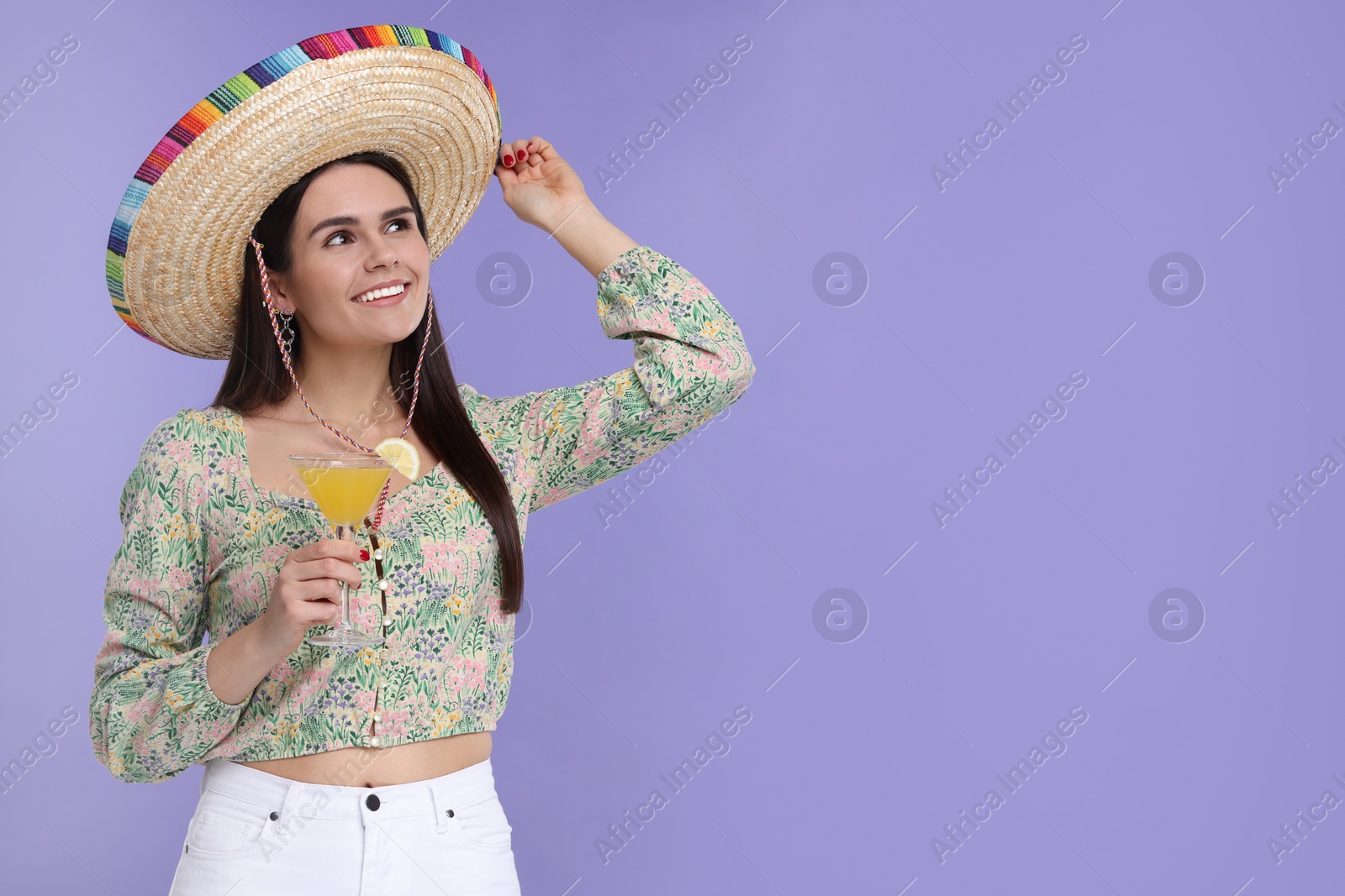 Photo of Young woman in Mexican sombrero hat with cocktail on violet background. Space for text