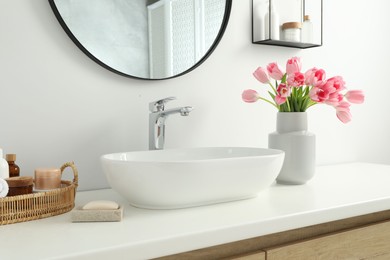 Photo of Vase with beautiful pink tulips and toiletries near sink in bathroom